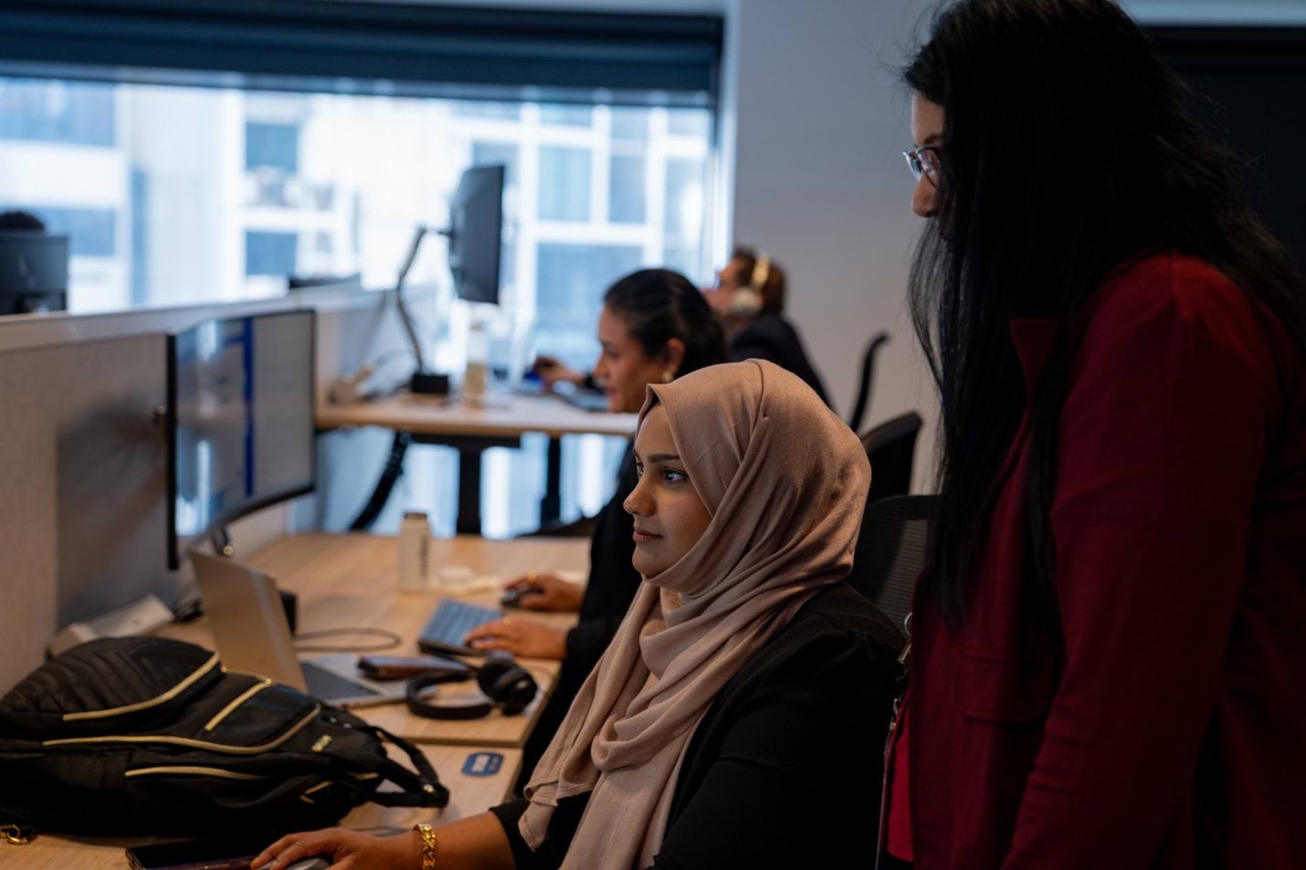 Woman standing next to another woman seated in front of a computer