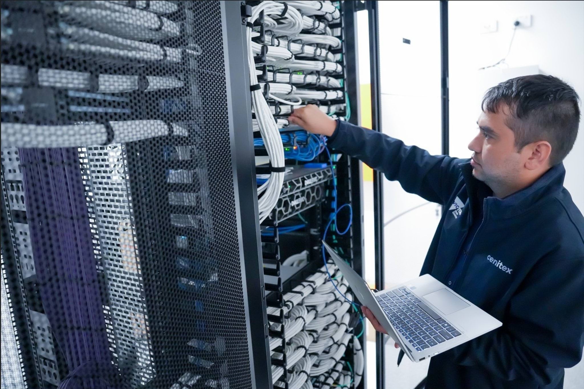 Man with laptop standing in front of server stack